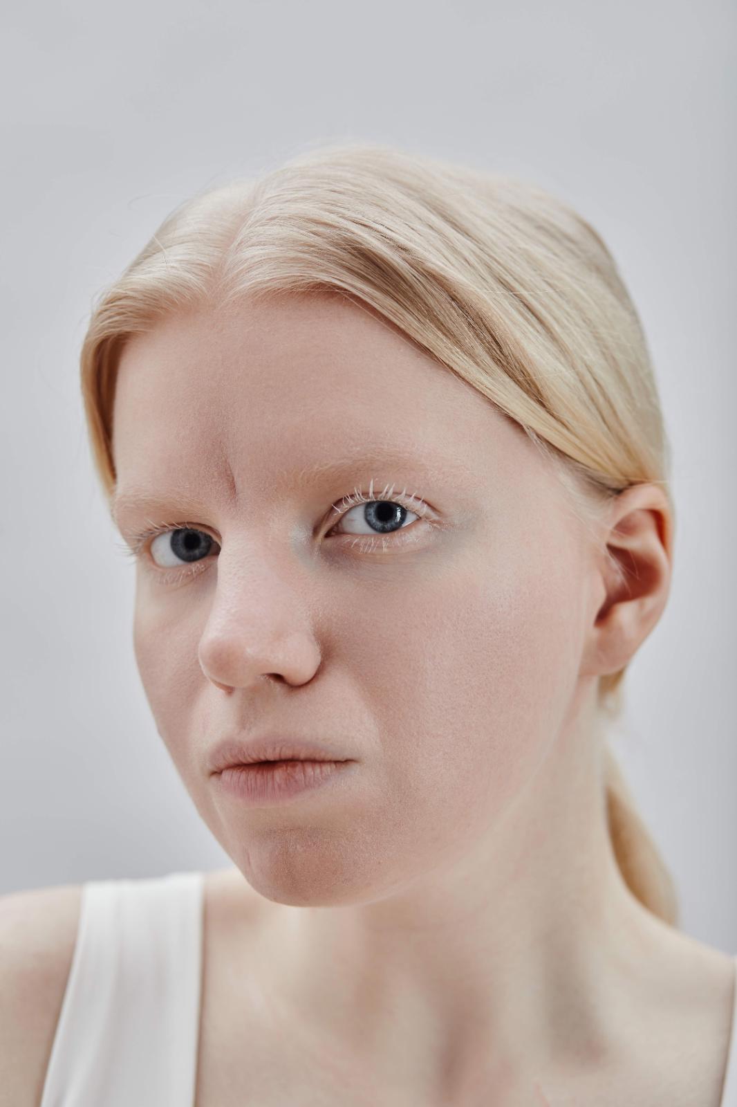 Close-up portrait of a woman with pale blonde hair and clear skin against a light grey background