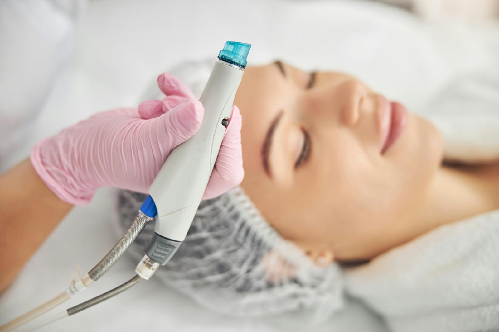 Close-up of an aesthetics provider holding a facial treatment handpiece beside a client resting during a professional skin treatment.