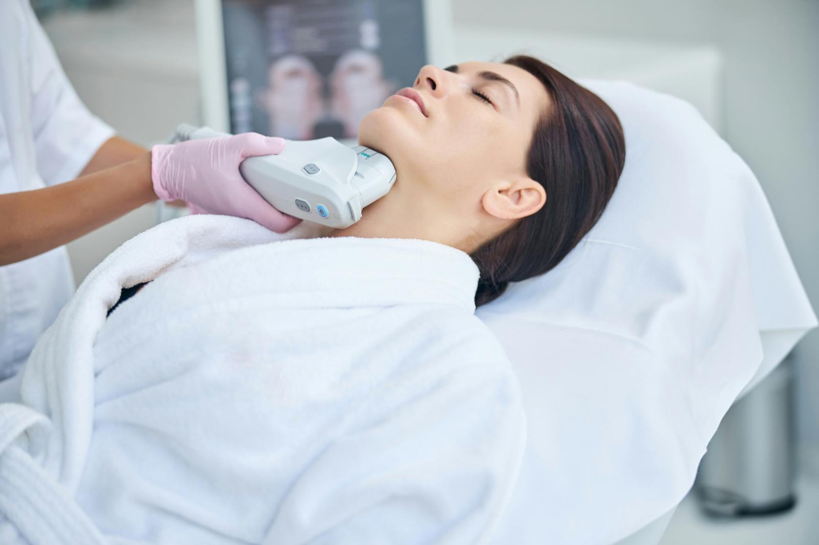 Client receiving a professional device-based treatment along the neck and jawline in a clinical aesthetics setting.