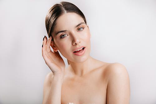 Close-up of an aesthetics provider holding a facial treatment handpiece beside a client resting during a professional skin treatment.